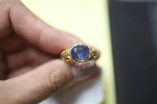 An antique yellow metal ring set with an oval sapphire in scroll-carved and pierced mount, size O.